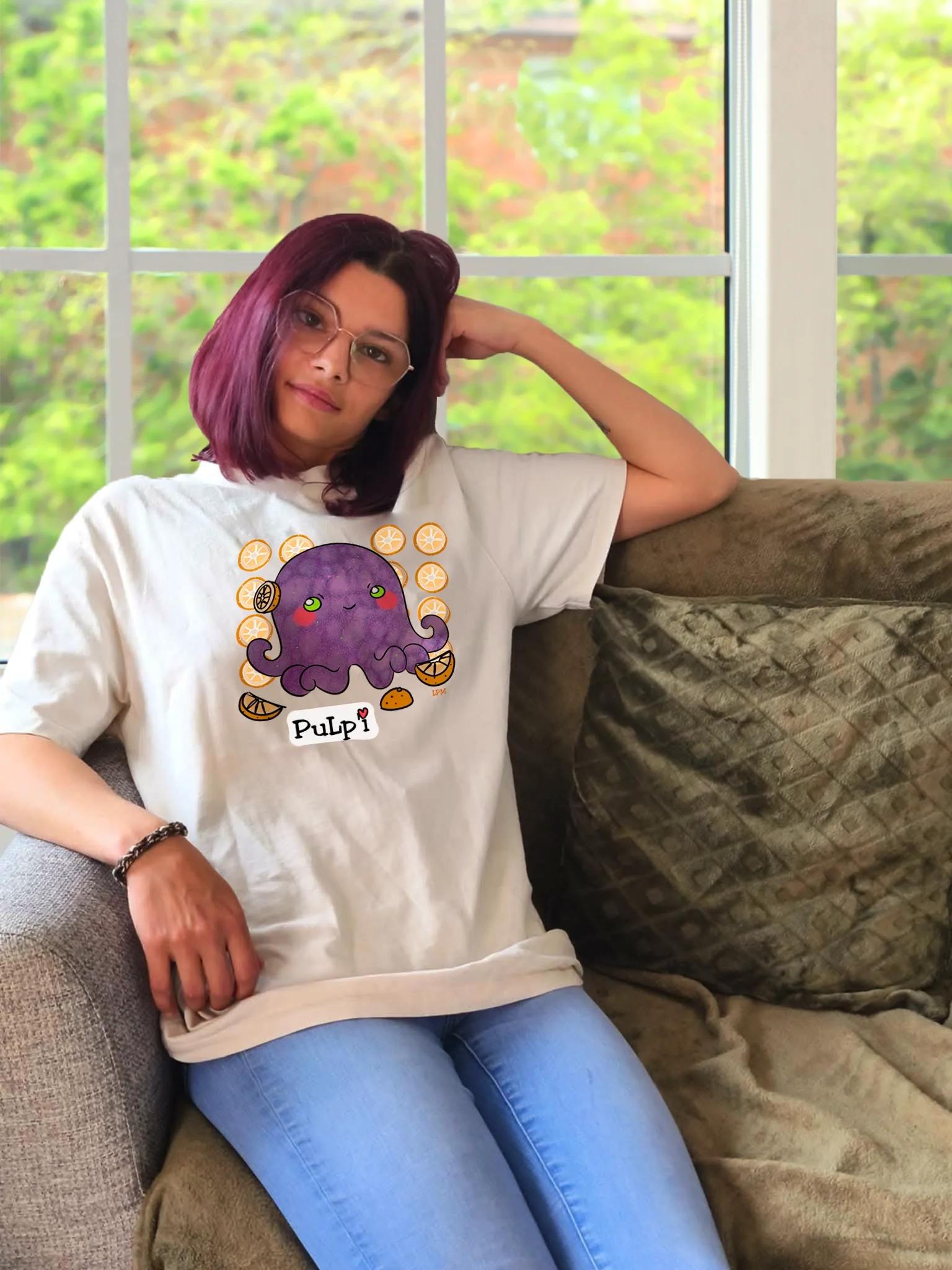 Une jeune femme dans un salon éclairé, assise dans un canapé confort qui porte un tee-shirt avec un design de Les pulls de Mama